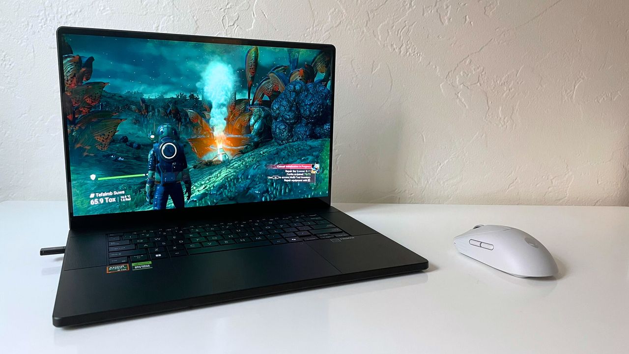 An open and powered on black laptop showing a video game, with a character in a spacesuit, on top of a white surface against a white wall, with a white mouse to the right of the laptop.