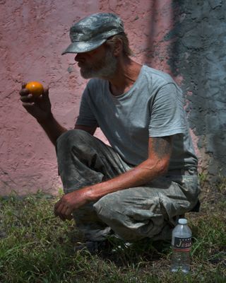 Man crouching and looking at an orange in his hand