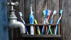 Manual and electric toothbrushes being stored in the bathroom near a tap