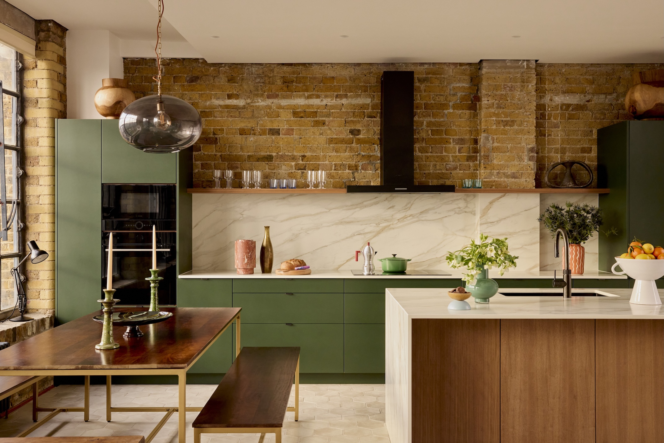 A large green and wood open plan kitchen zoned into cooking and dining areas