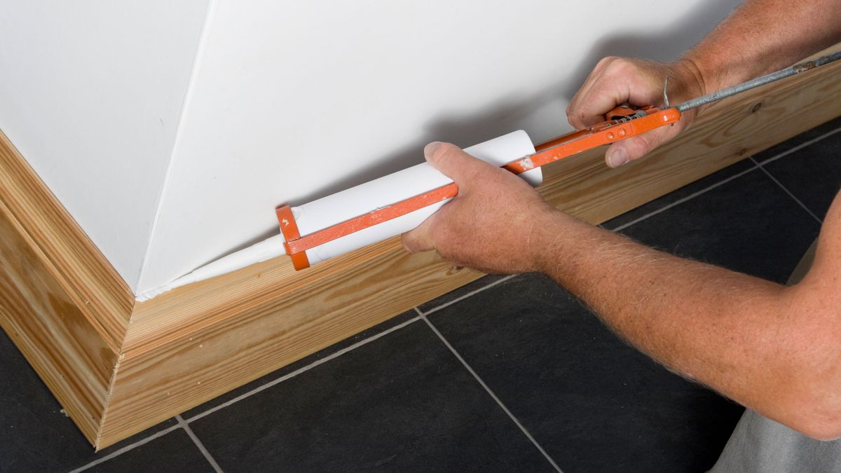 Man caulking skirting boards with caulking gun