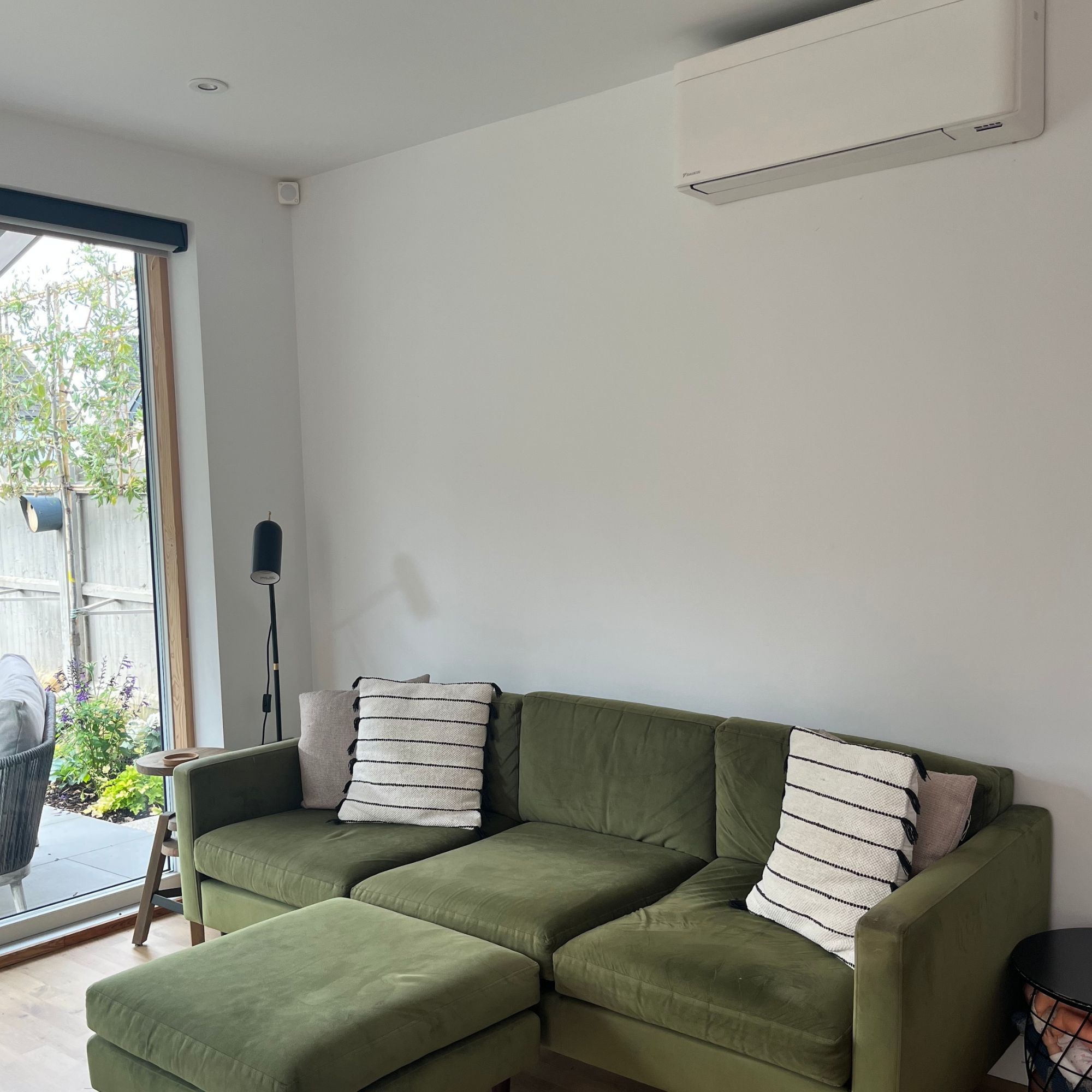 Fitted air conditioning unit on a neutral wall above a moss green sofa with monochrome striped cushions