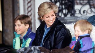 Princess Diana, Prince William and Prince Harry sitting in a sleigh with blankets and wearing bright ski coats in the 1990s