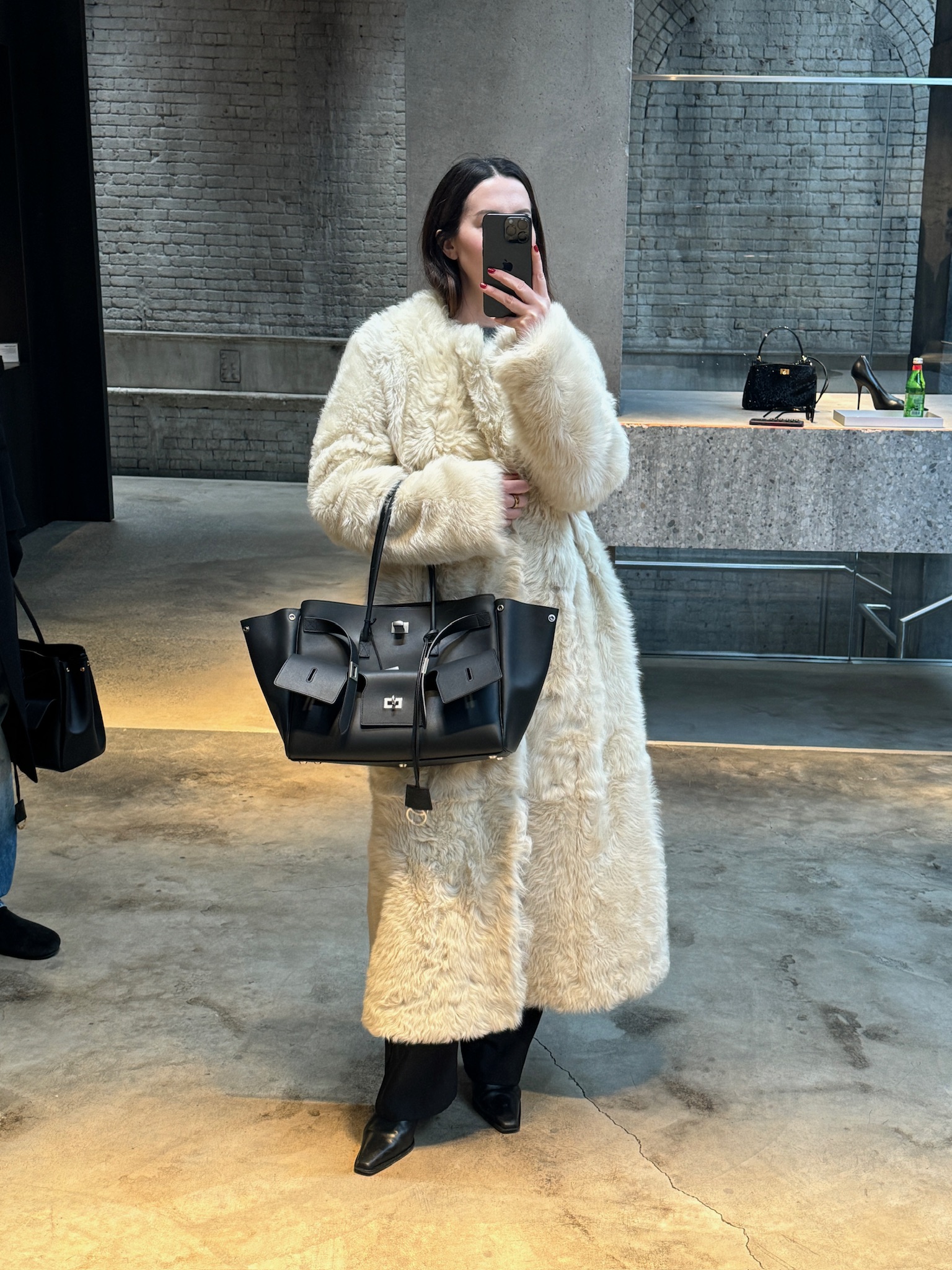 Caitlin Burke wearing an off-white shearling coat and carrying a Balenciaga Bel-Air Carry All in black with silver hardware.