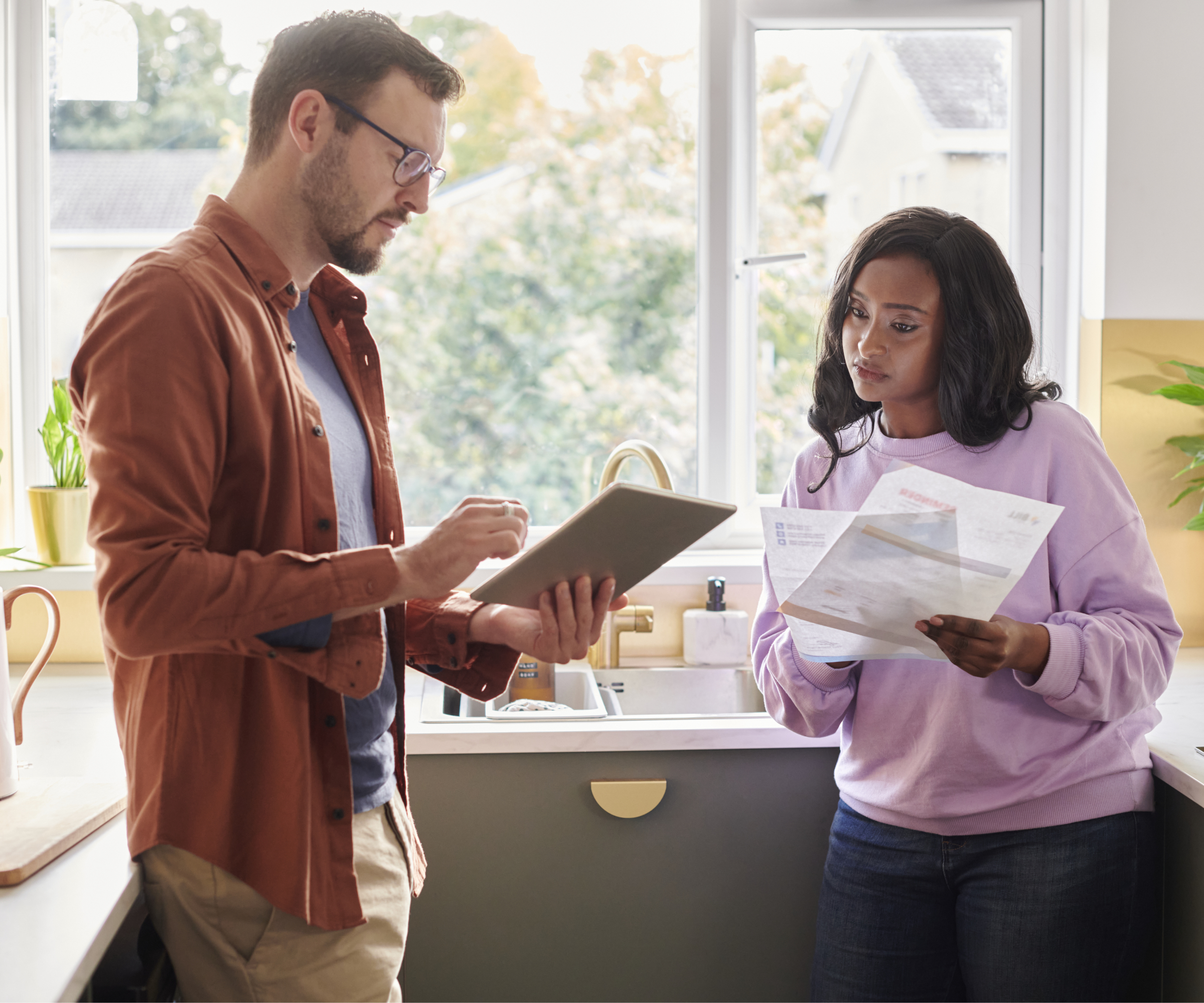 male and female stood in kitchen comparing documents