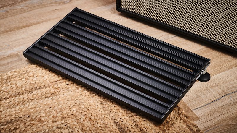 An Aclam Smart Track S2 pedalboard on a rug in front of a guitar amp