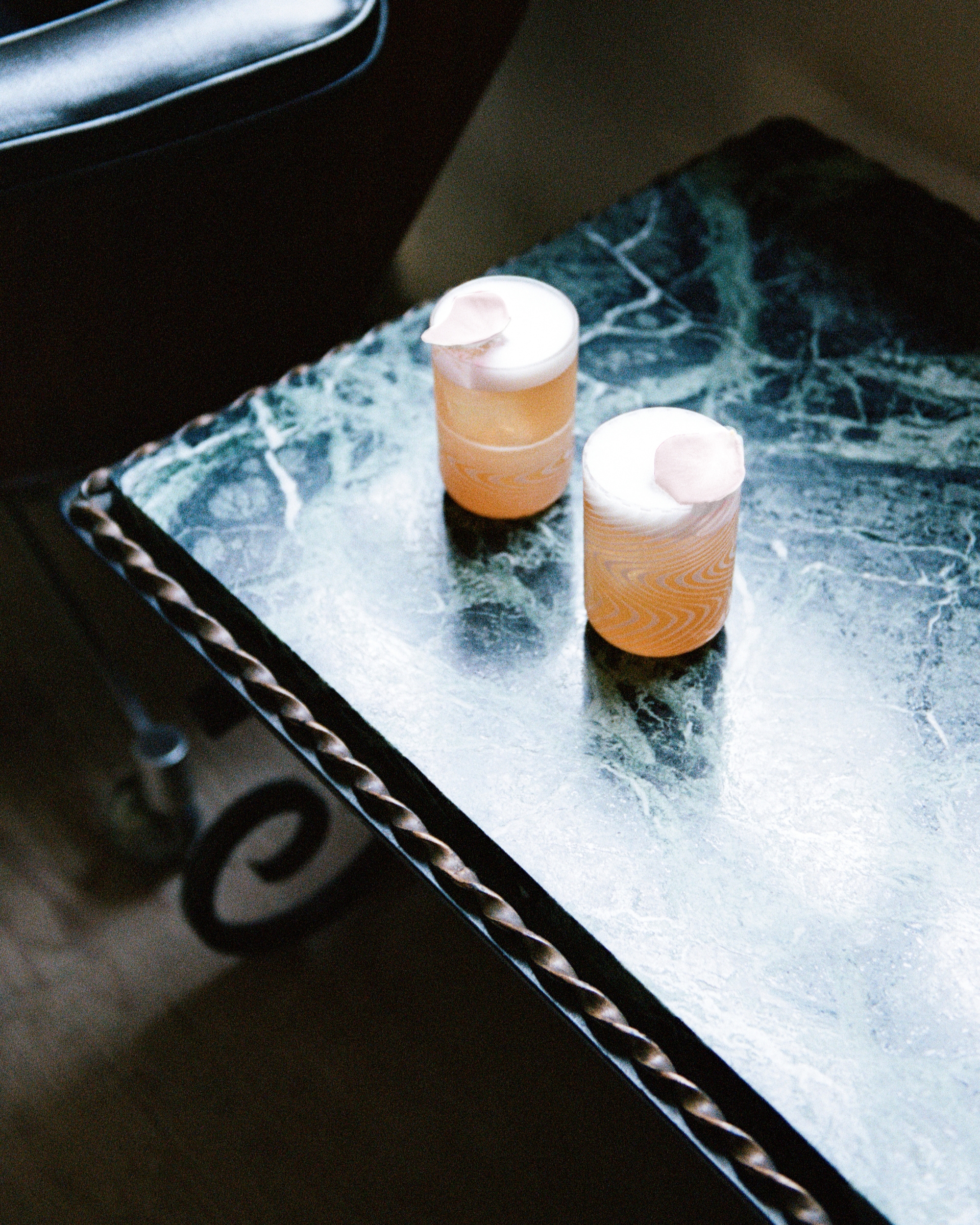 Image of two orange cocktails sitting on a blue marble coffee table in a dark room.