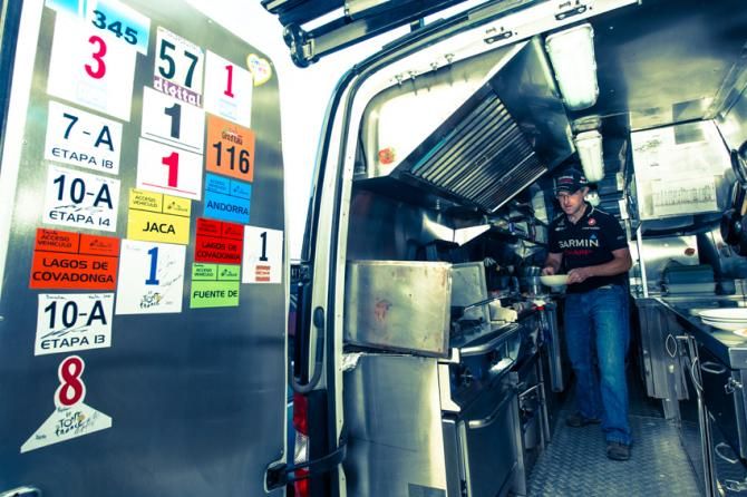 Sean Fowler whips up breakfast in the back of his van with the doors decorated with accreditation badges from previous races.
