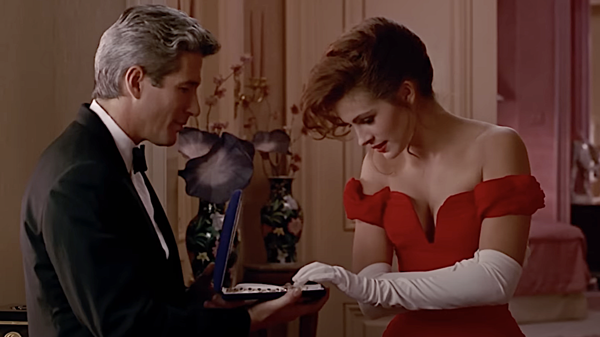 Richard Gere holding out a jewelry boy to Julia Roberts wearing a red dress in Pretty Woman