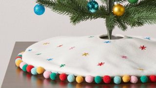 A white mini tree skirt with colorful embroidered snowflakes and colorful bordered pom poms
