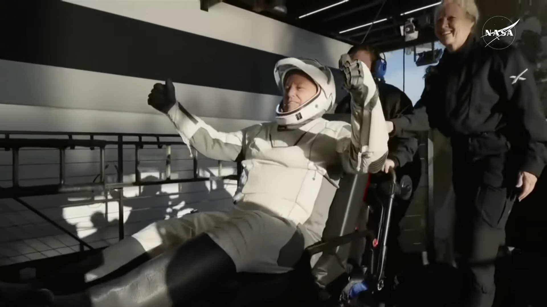 A male NASA astronaut in a white and black spacesuit raises both arms in triumph after leaving his Crew-9 spacecraft on stretcher 