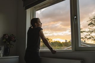 Woman looking out of her window as the sun sets