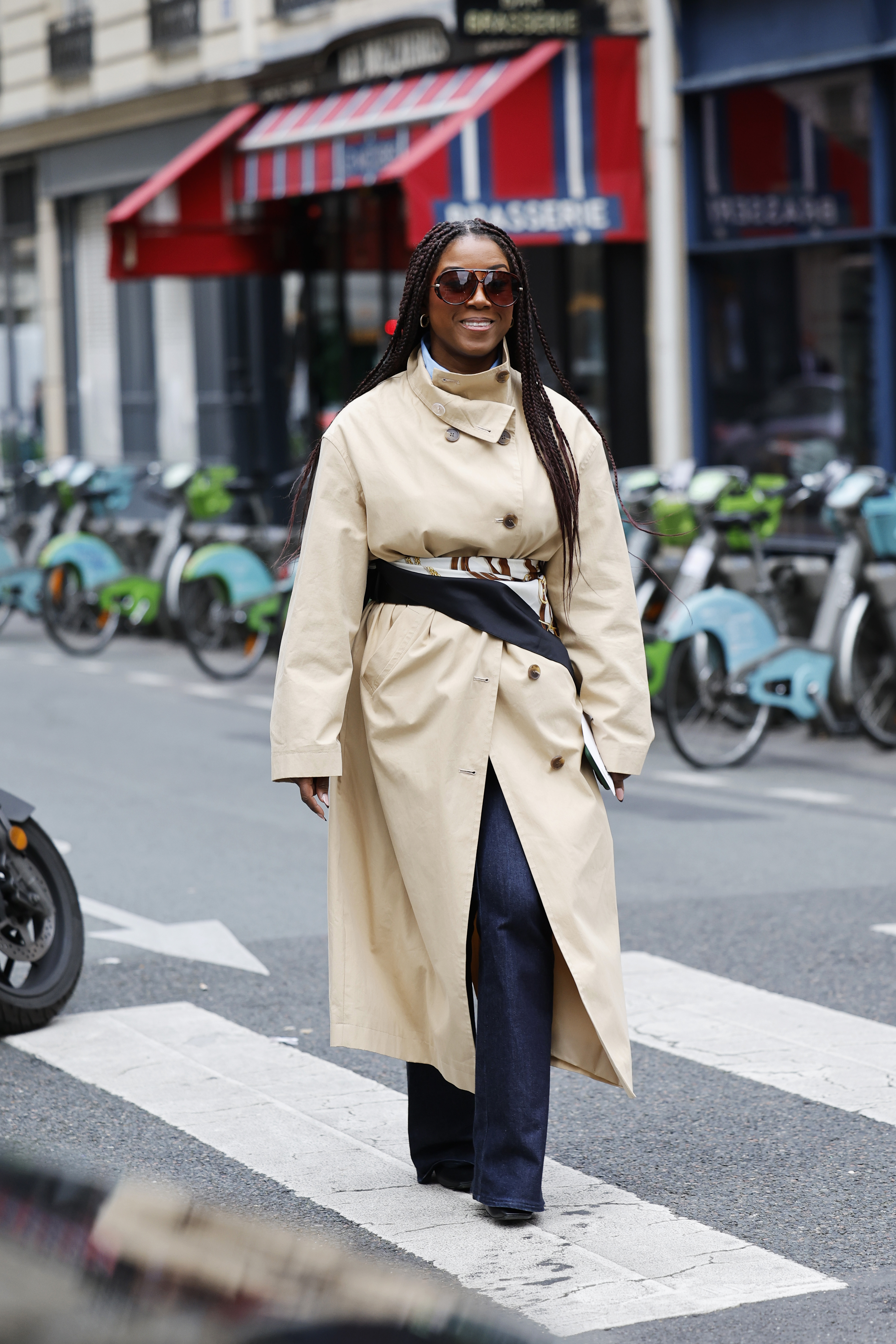 PARIS, FRANCE - OCTOBER 06: Angela Baidoo wears beige trench coat, black white brown printed silky scarf as belt, dark wash jeans, outside Sacai, during the Womenswear Spring Summer 2026 as part of Paris Fashion Week on October 06, 2025 in Paris, France. (Photo by Claudio Lavenia/Getty Images)