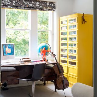 home office with white wall and yellow canbinet and desk with violin and globe