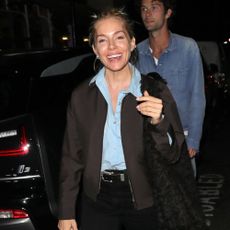 Sienna Miller steps out in London wearing black jeans with square-toe flats, a blue shirt and a dark brown jacket.