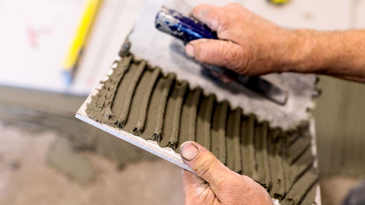 Close of person applying tile adhesive to back of tile