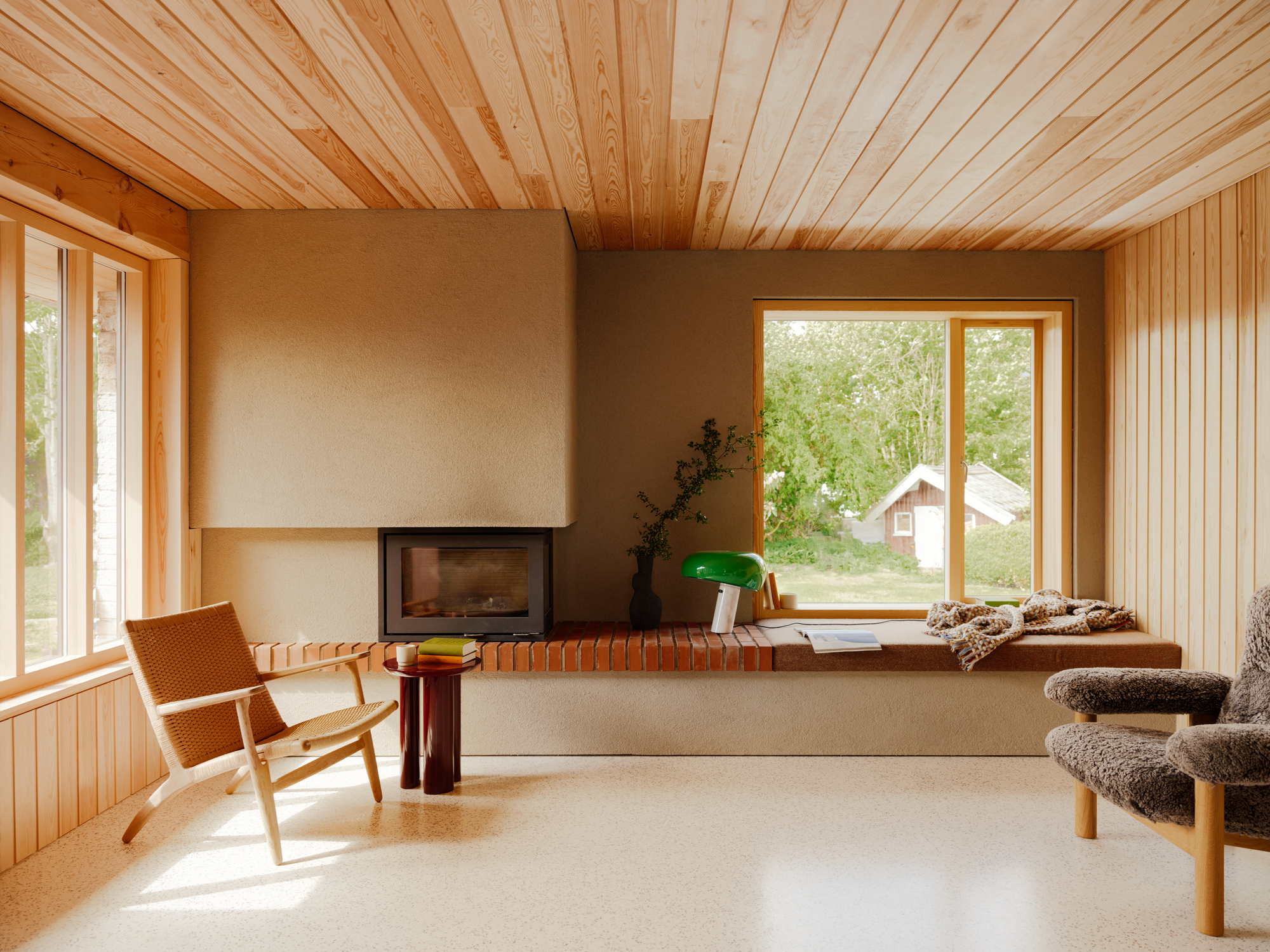 A modern minimalist living room with a scandi-style influence, including a fireplace, a leather accent chair, and a green lamp on the windowsill