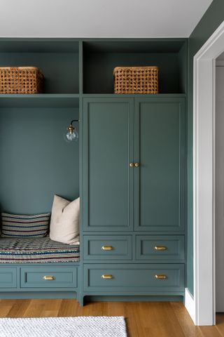 Dark teal wood built-in entryway storage with cushions and wicker baskets.