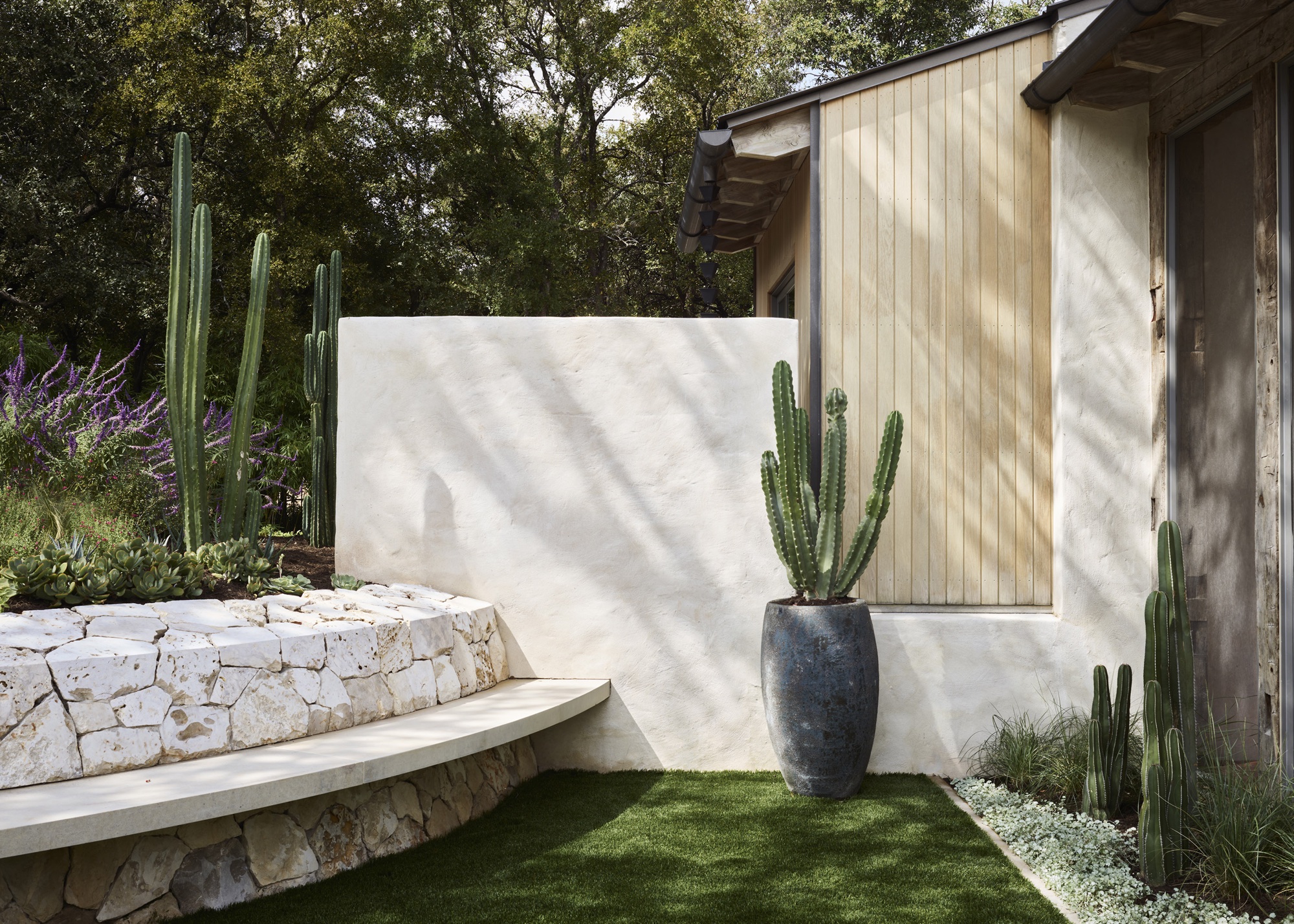 low stone wall with built-in seating in small garden with a small cactus plant in a grey pot beside a wall