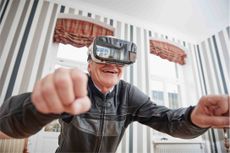 An older man wearing a VR headset, as an example of how technology helps retirees live at home. 