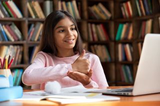 Smiling girl makes sign language gesture with laptop computer