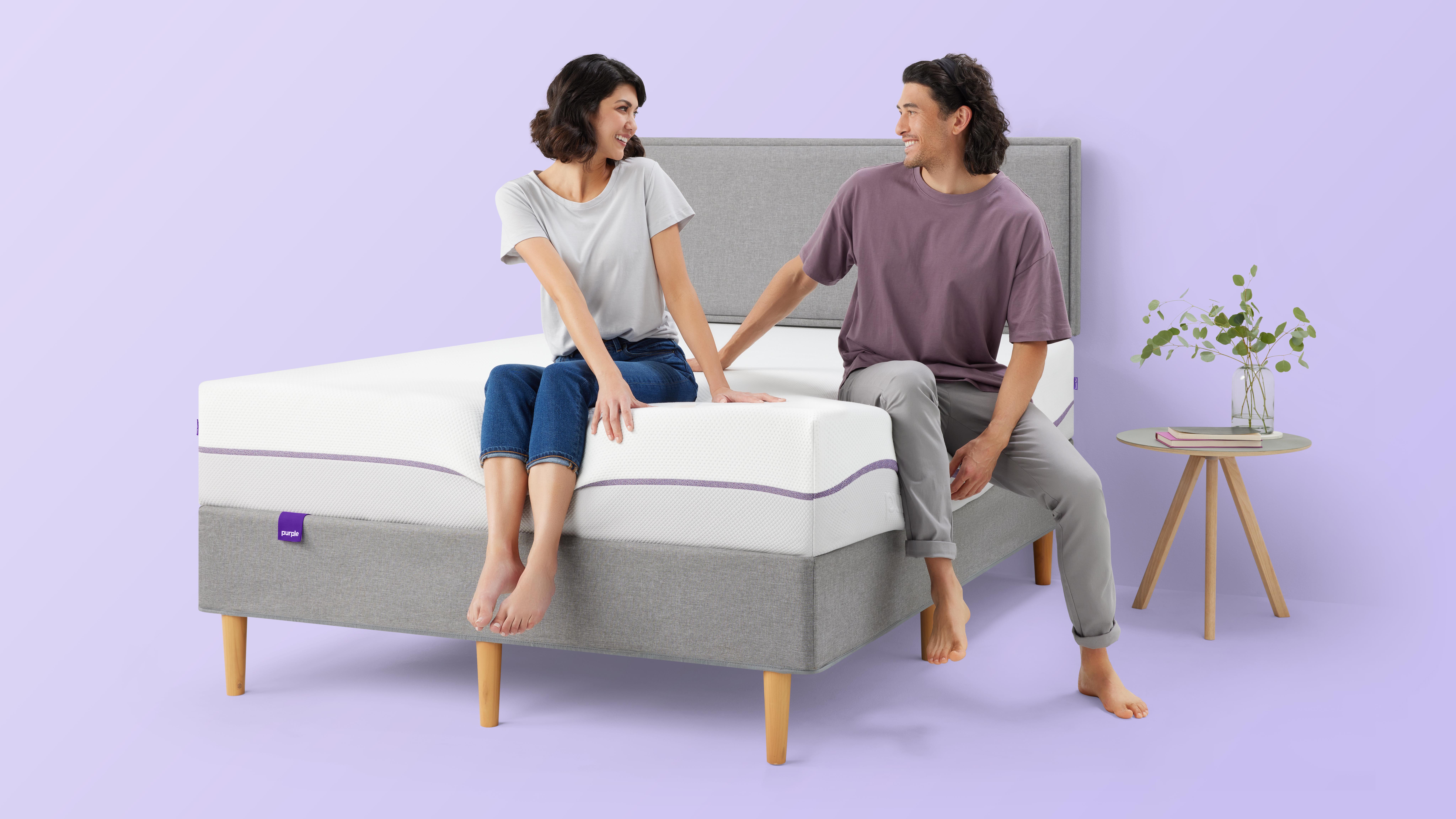 Purple Plus Mattress review: A man and a woman talk and laugh while sat on the edge of the Purple Plus mattress