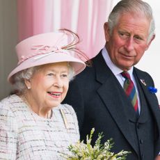 Queen Elizabeth wears a white tweed coat and a pink hat while her son Prince Charles wears a navy suit with a blue and red tie