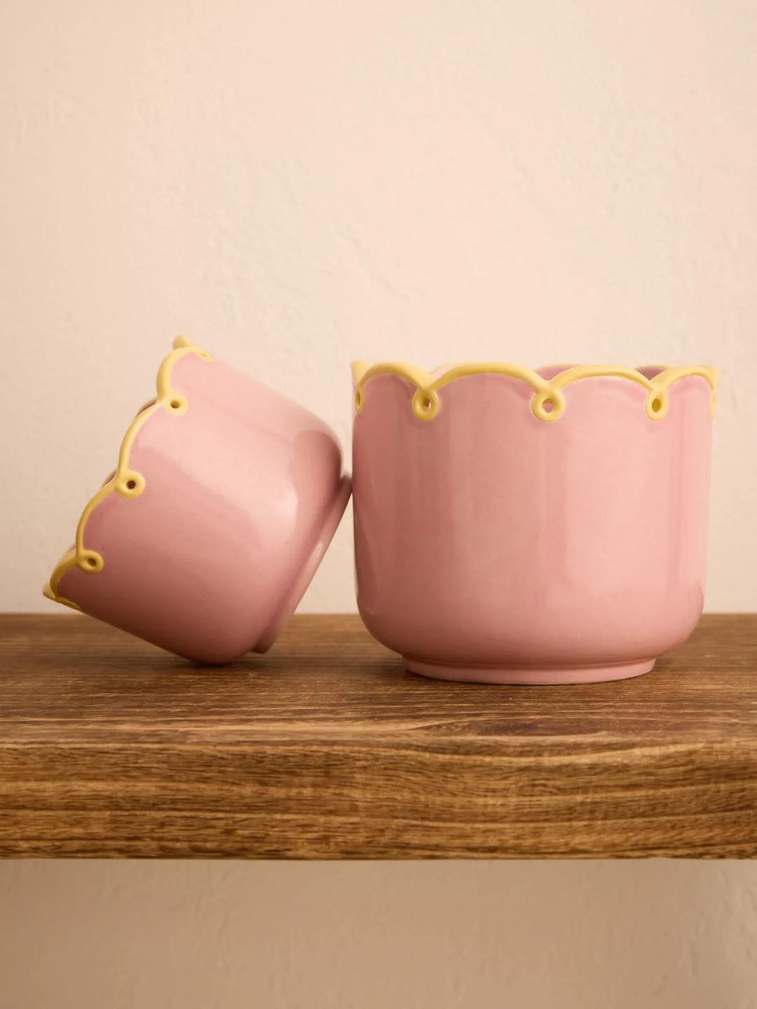 A pink scalloped planter with a yellow rim
