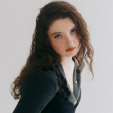 the testaments star lucy halliday poses in a head shot wearing an argylle sweater and leaning forward against a white backdrop