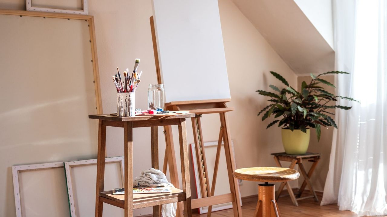 An artist eisle with a canvas frame on it next to a small table of paint brushes and paint