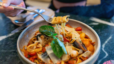 Asian woman eating a plate of seafood pasta on a table