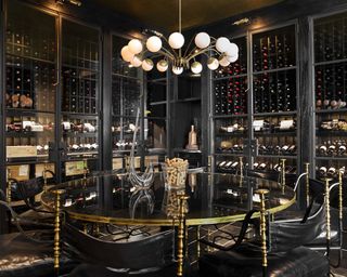 Modern dining room ideas with black walls filled with wine racks and cabinets, mirrored circular table, gold and black chairs and globe chandelier
