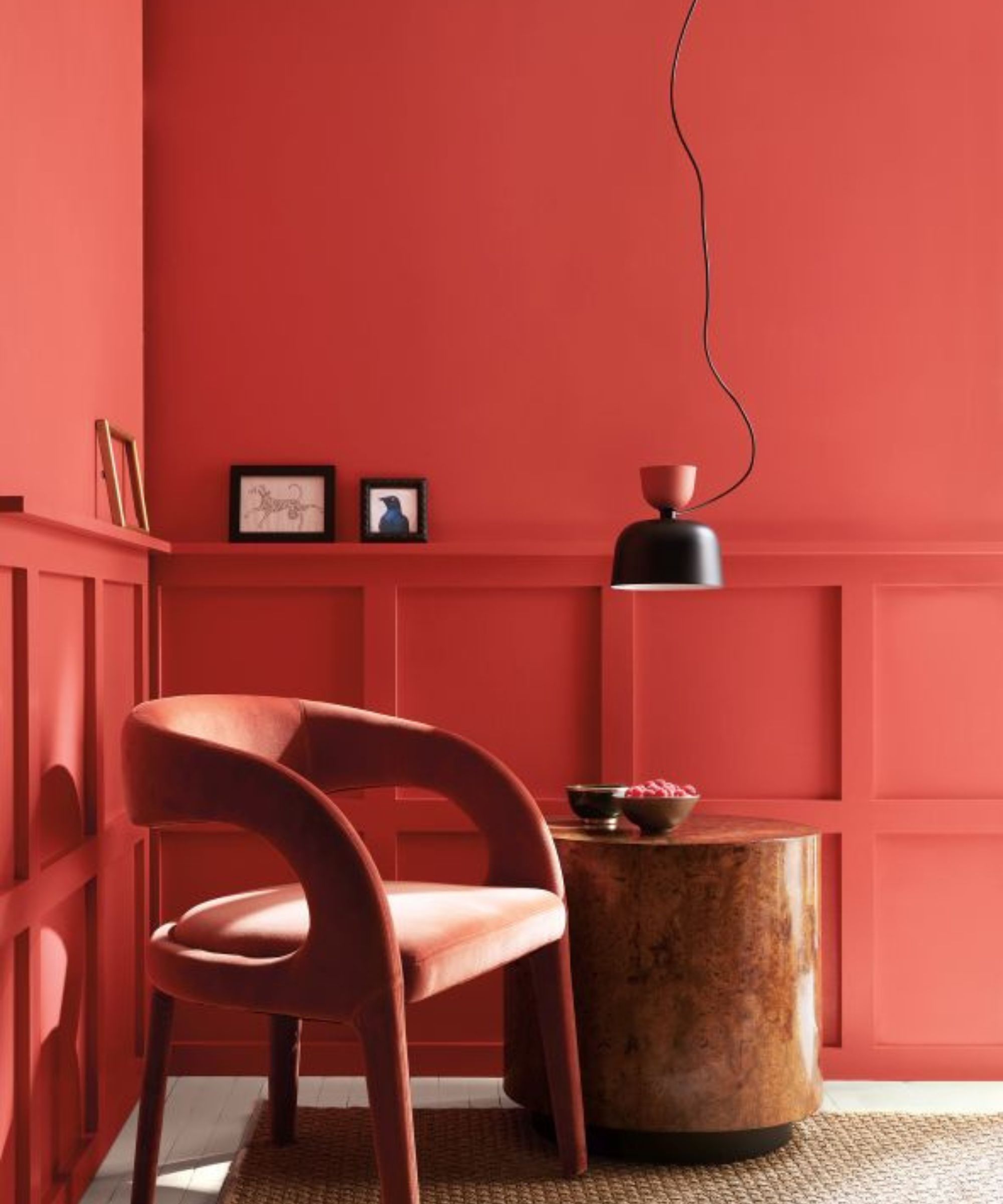 Living room painted in a bright red paint with wall panelling, velvet red armchair, burl wood side table, pendant light and art on walls