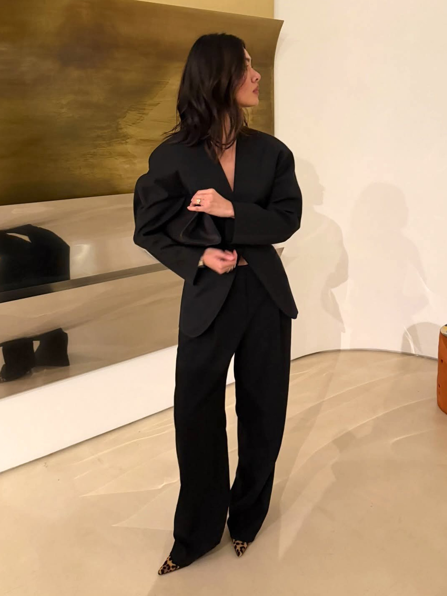 style influencer Mimi Nguyen poses in a black fitted blazer, a black clutch, black trousers, and leopard-print heels