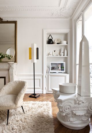 white apartment living room with fluffy chair and rug, contemporary floor lamp, ornaments and vases in alcove shelving, gold vintage mirror, herringbone floor