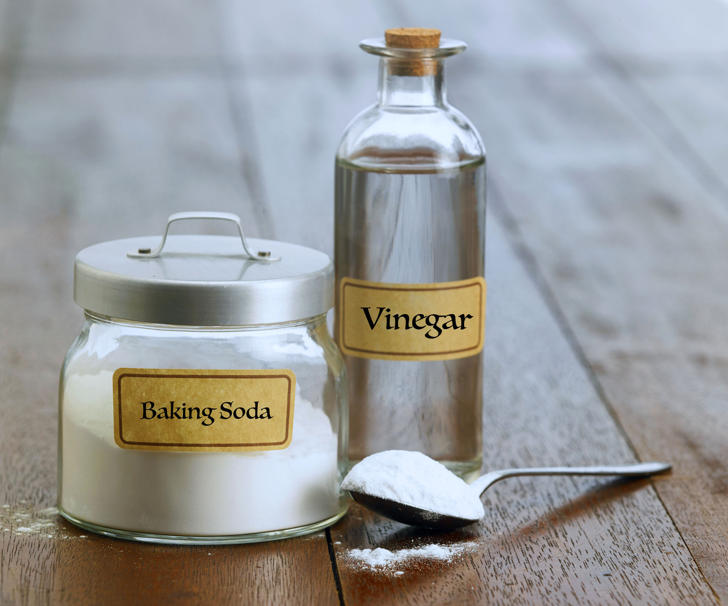 containers of baking soda and vinegar on wooden surface with spoon of baking soda