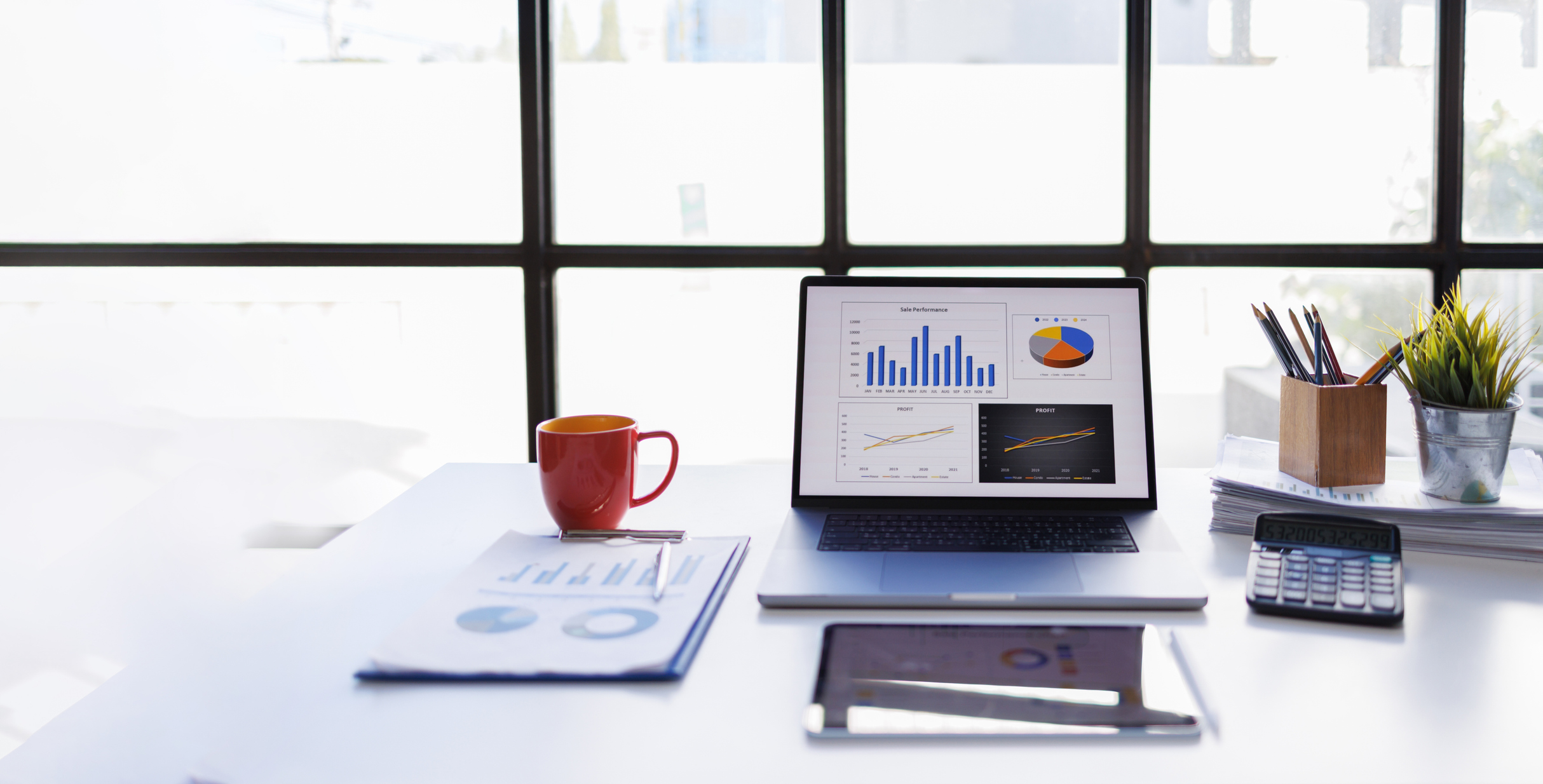a desk with a coffee cup, financial projections and an open laptop with bar graphs and pie charts