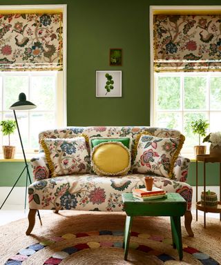 A fall color scheme in a living room with olive green walls and natural patterned white fabric on sofa and blinds