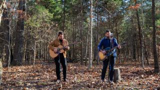 Wade Bowen and his guitar player playing music in the woods.