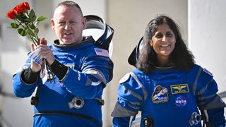 two astronauts in spacesuits. the man on the left holds roses