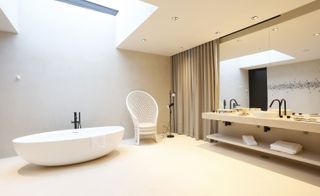 Interior view of the Montebelo Vista Alegre bathroom. Wide tub with a skyline window above it, sink area to the right with a mirror that goes up to the ceiling.