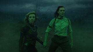 Sophia Di Martino and Tom Hiddleston hold hands while standing bathed in green light in Loki Season 1.