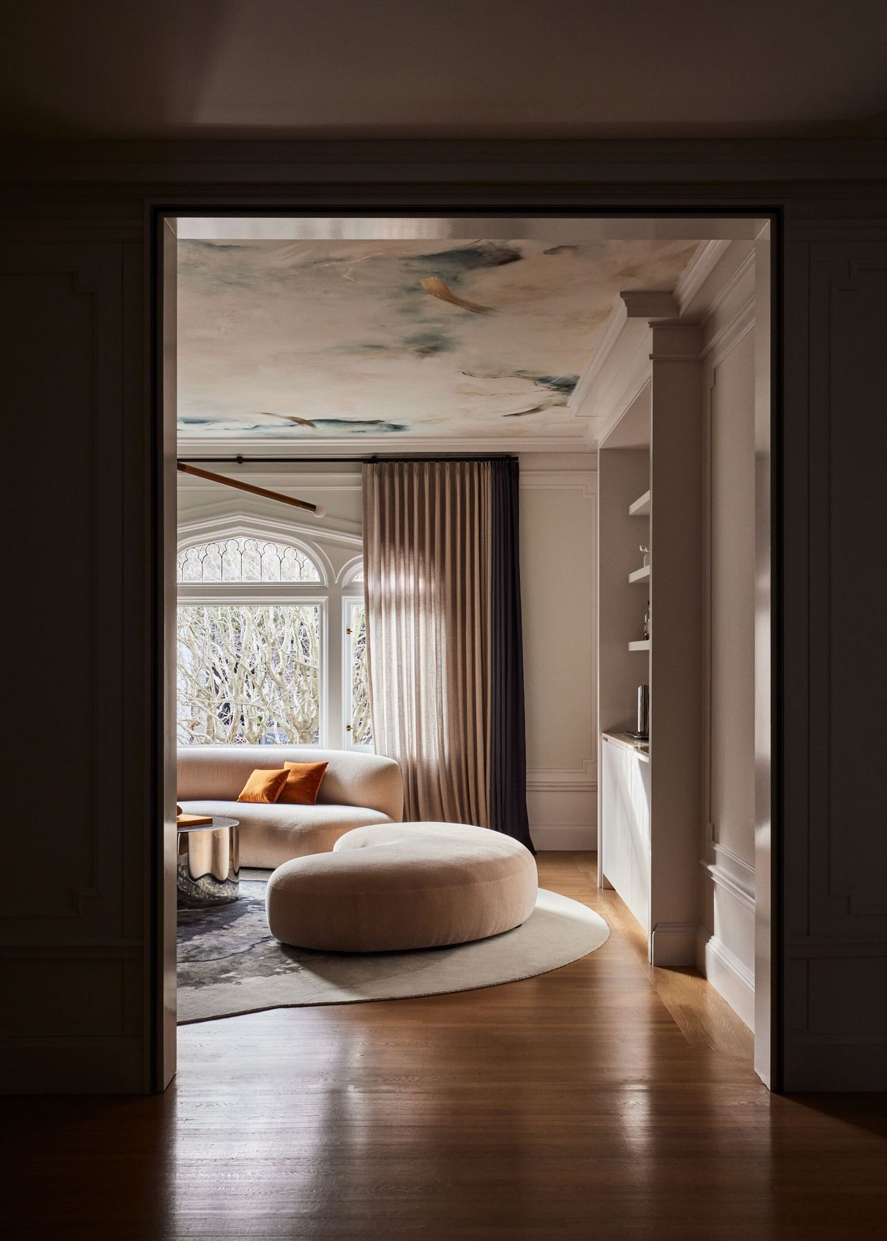 The view of the renovated living room from through the doorway showcasing its bespoke ceiling mural and curved couch
