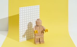 A lego character made from wood on a yellow canvas.