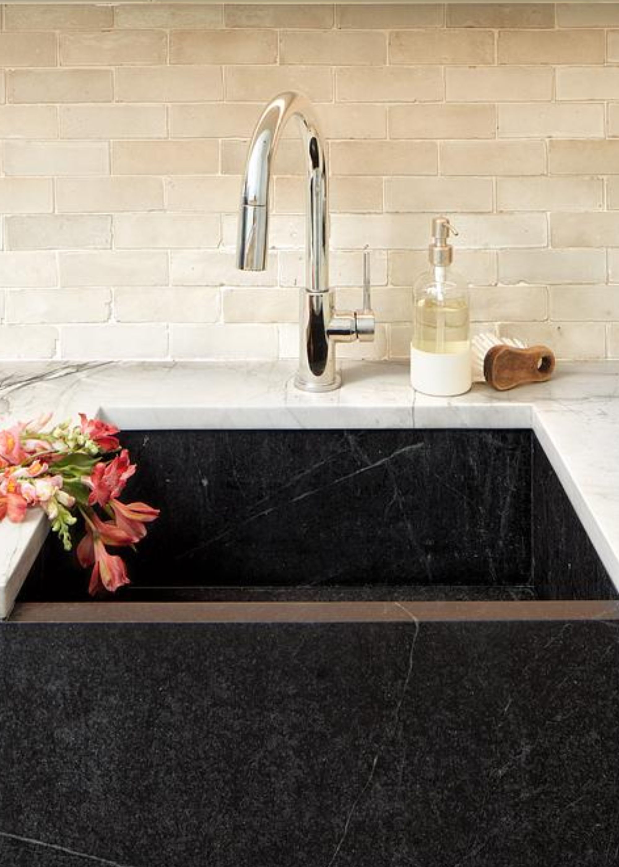 A sink made from soapstone with a silver tap and soap beside it as well as a brush. There are also flowers hanging beside the sink