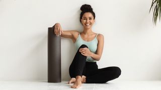 a photo of a woman holding a yoga mat sat next to a wall 