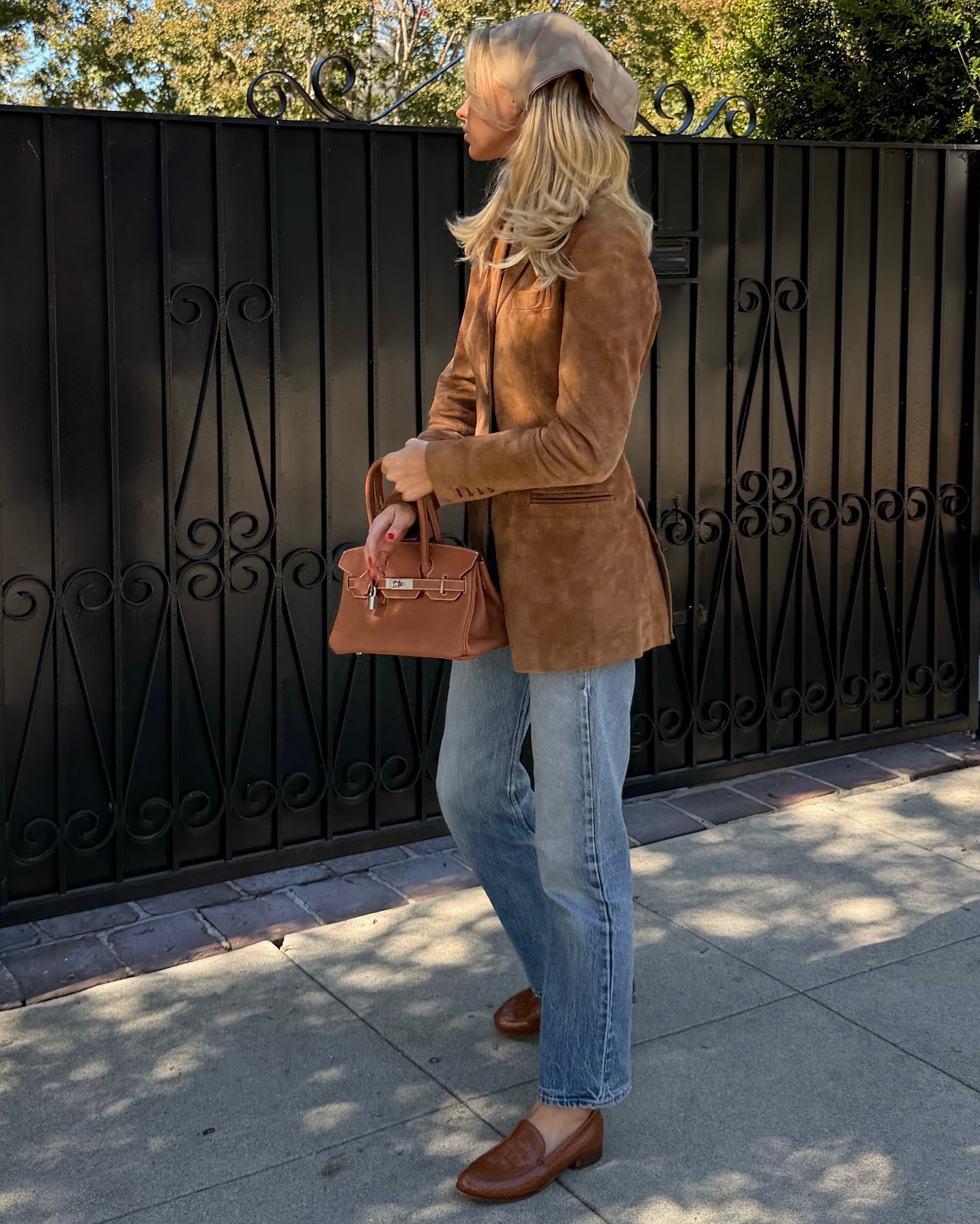 Model Elsa Hosk poses for a photo outside wearing a brown suede jacket with brown loafers, a brown Hermes bag and light-wash blue jeans.
