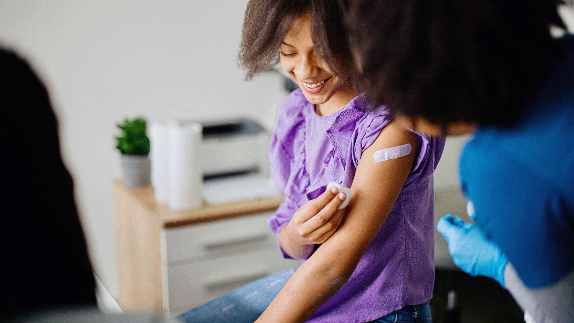 A woman with dark curly hair puts a band aid on her arm