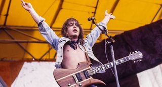 Rick Derringer throws his hands in the air as he performs live with a B.C. Rich Mockingbird in 1977