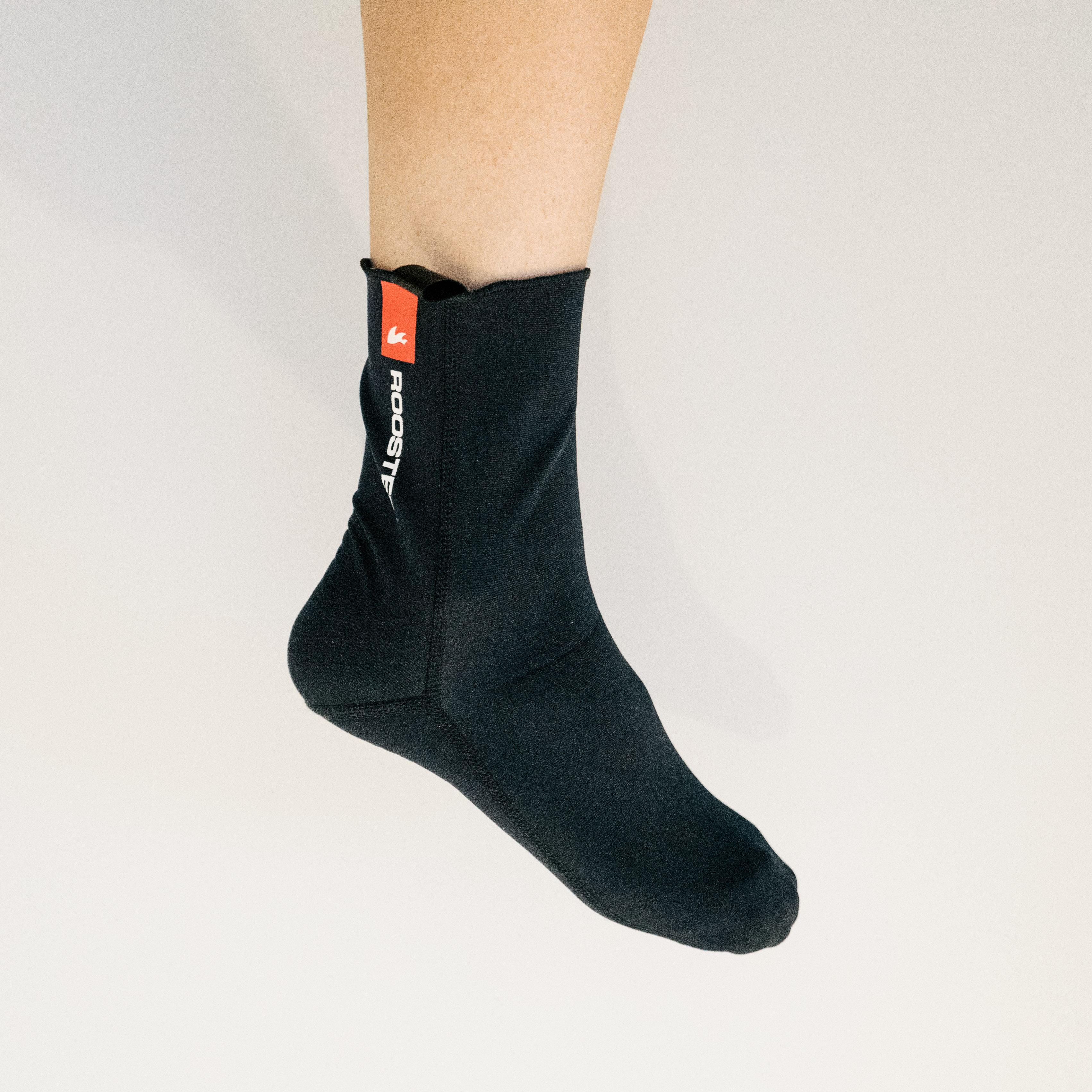 A white leg wears a black neoprene cycling sock against a white background